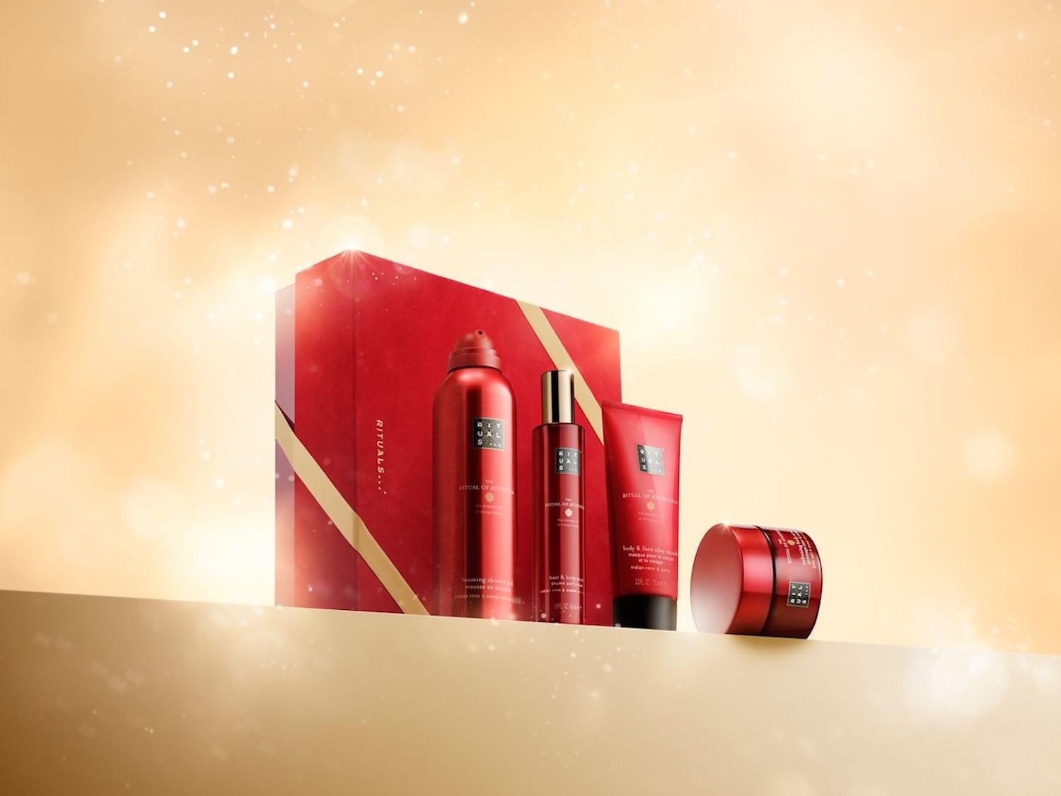 Ein rotes The Ritual of Ayurveda Geschenkset von Rituals mit Duschschaum, Haarspray, Tonmaske und Körpercreme vor einem festlichen, goldenen Hintergrund. Jetzt entdecken und Freude schenken!