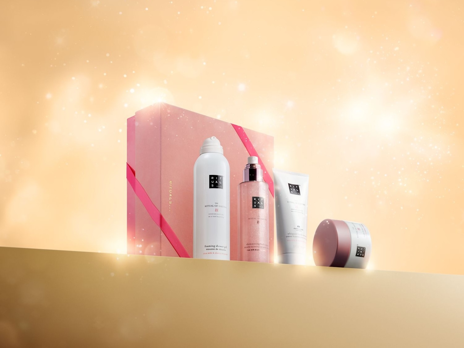 Ein wunderschönes Geschenkset von Rituals mit verschiedenen Pflegeprodukten in zarten Rosatönen vor einem funkelnden Hintergrund. Jetzt entdecken und Freude schenken!