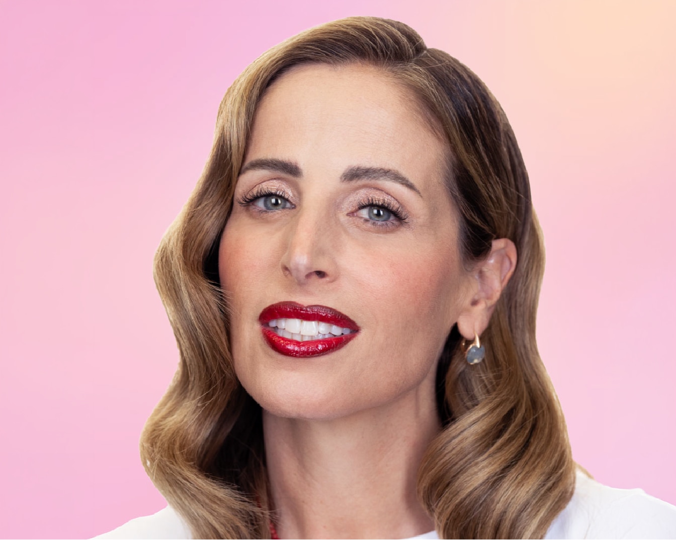 Una donna con capelli castani ondulati, labbra rosse lucide e un leggero trucco sugli occhi, indossa un orecchino pendente su sfondo rosa.