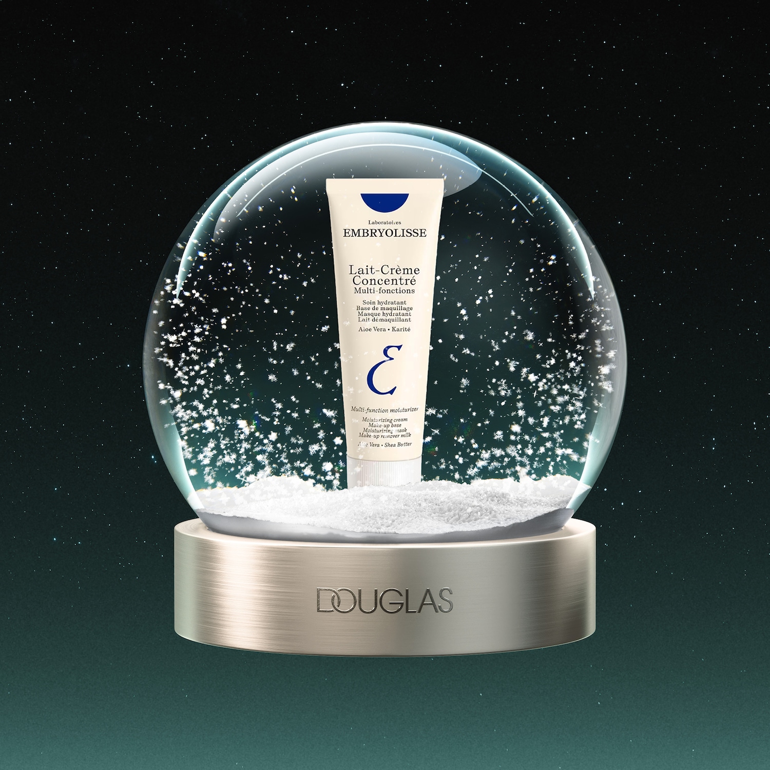 Een Embryolisse Lait-Crème Concentré Multi-fonctions tube staat in een sneeuwbol met de tekst "DOUGLAS" op de gouden voet, tegen een donkerblauwe sterrenhemel.