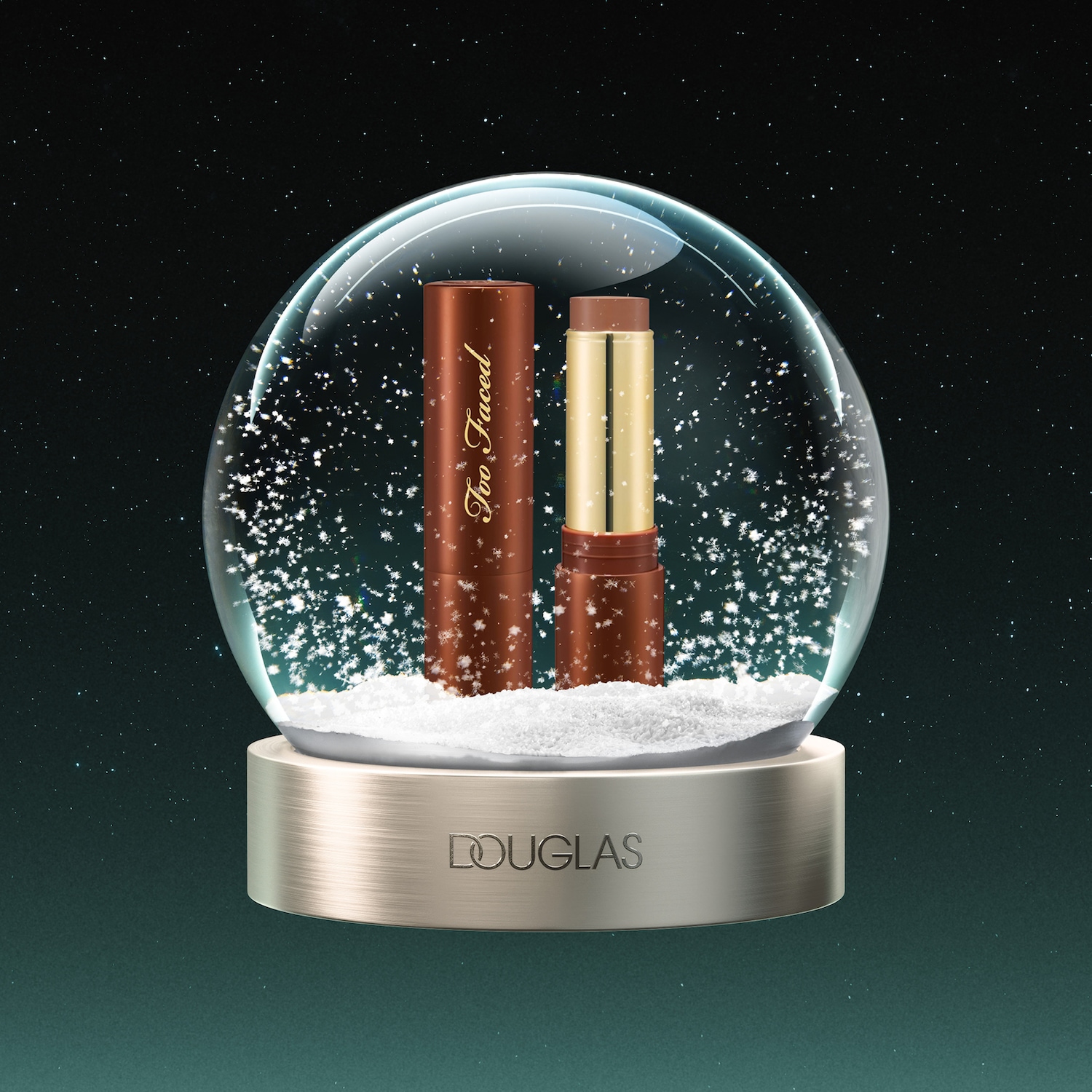 Een Too Faced contourstick in een glazen sneeuwbol met de merknaam Douglas op de gouden voet, omringd door vallende sneeuwvlokken tegen een donkergroene, sterrenhemelachtergrond.