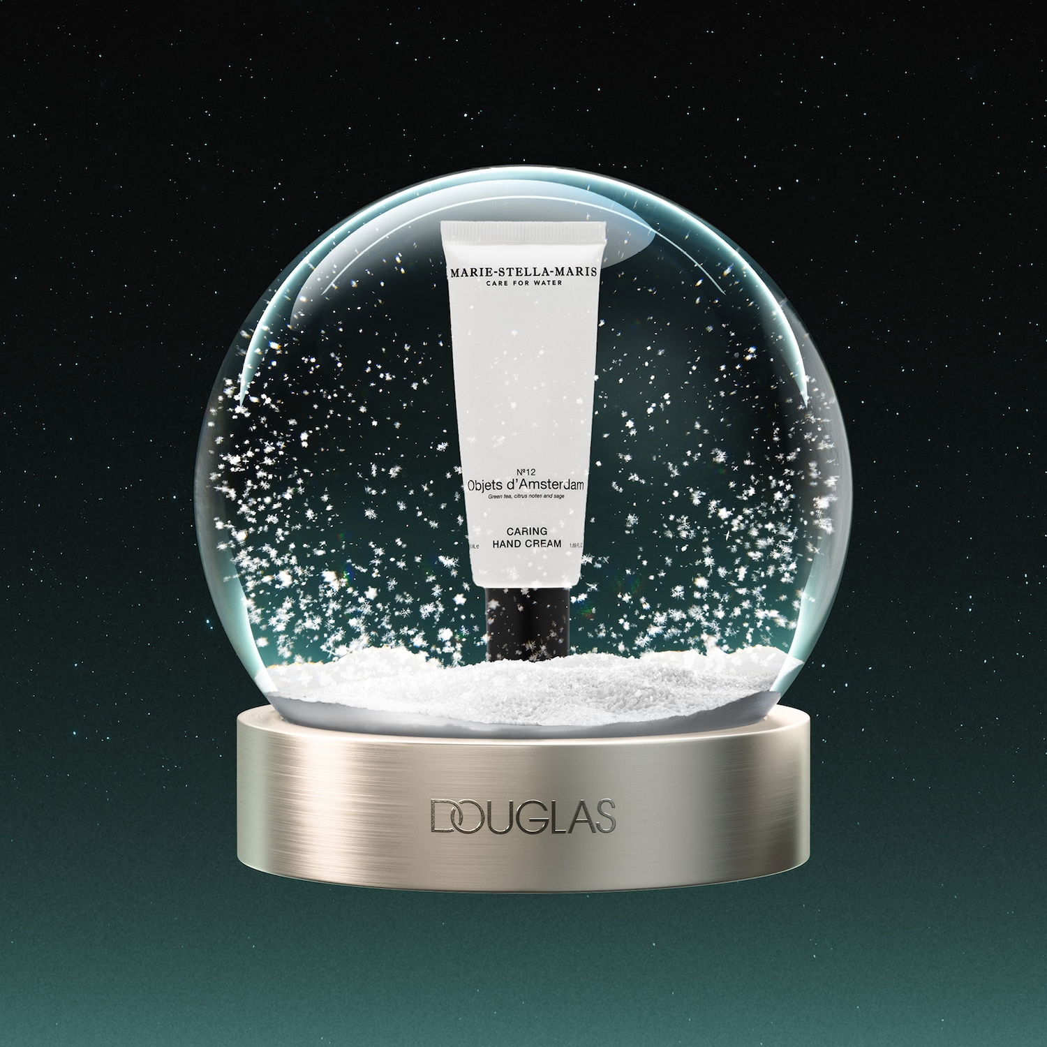Een Marie-Stella-Maris handcrème in een sneeuwbol met de tekst "Nº12 Objets d'Amsterdam, Green tea, citrus notes and sage, CARING HAND CREAM" en het Douglas-logo op de basis.
