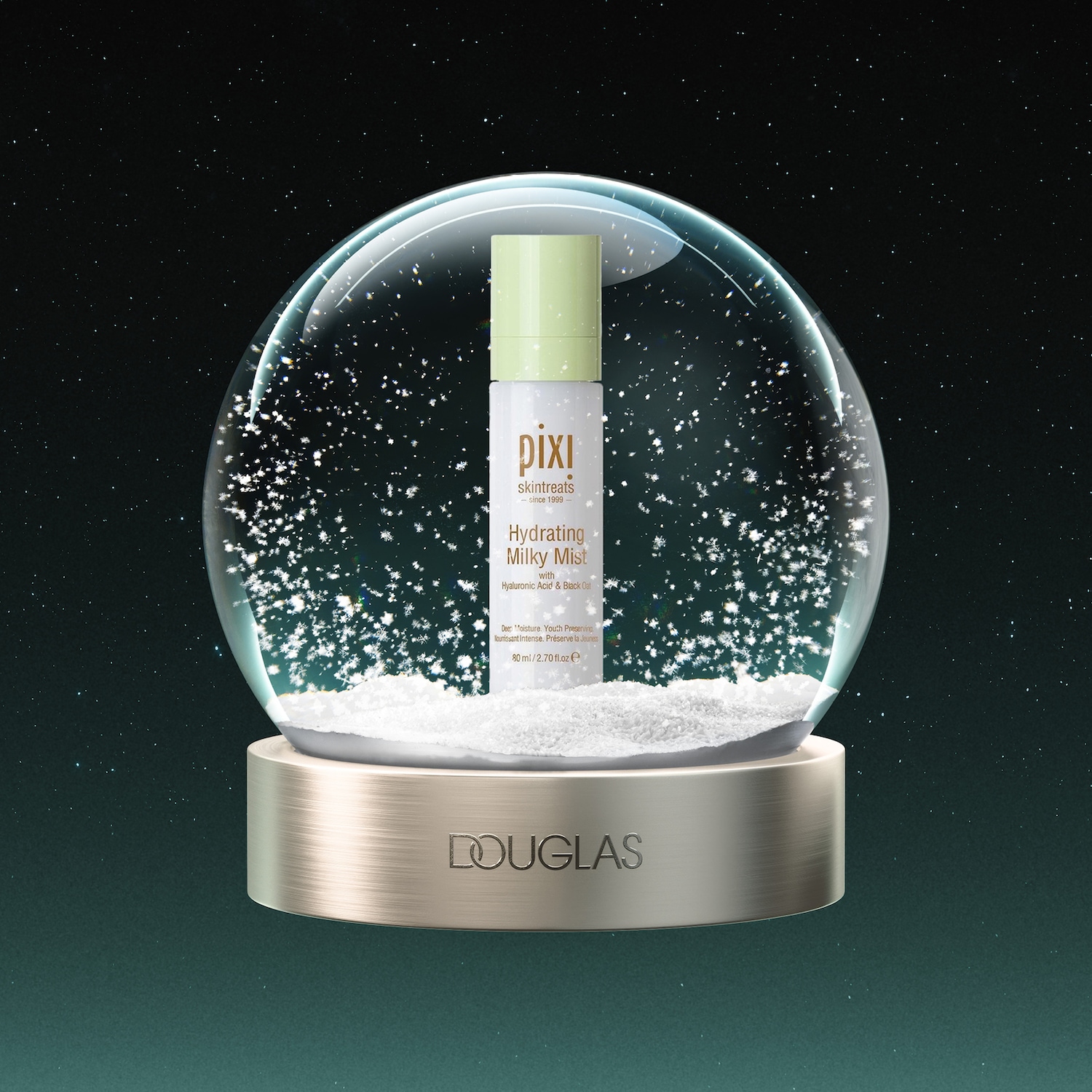 De Pixi Hydrating Milky Mist, een witte fles met lichtgroene dop, staat in een glazen sneeuwbol gevuld met witte sneeuwvlokken, op een gouden voet met het Douglas-logo, tegen een donkerblauwe sterrenhemel.