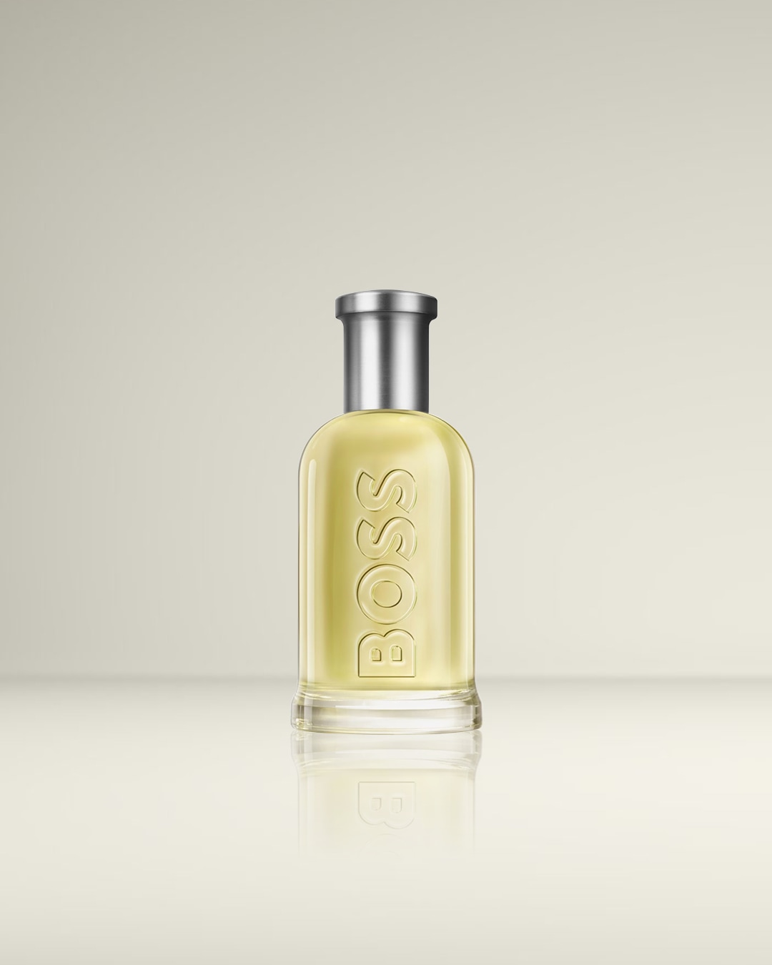 Een BOSS parfumflesje met een zilverkleurige dop en een lichtgele vloeistof, met de naam "BOSS" verticaal in reliëf op de voorkant van de fles.