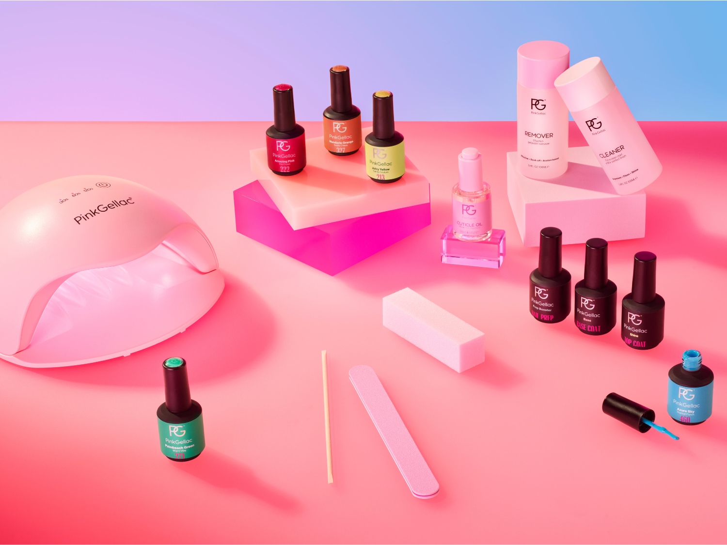 Un ensemble complet de vernis à ongles Pink Gellac est présenté, comprenant une lampe UV rose, des vernis de différentes couleurs comme le rouge, l'orange, le vert, le jaune et le bleu, ainsi que des produits de soin comme le dissolvant, le nettoyant, l'huile à cuticules, le préparateur, la base et le top coat, accompagnés d'une lime à ongles et d'un bâtonnet en bois, le tout disposé sur un fond rose et bleu.