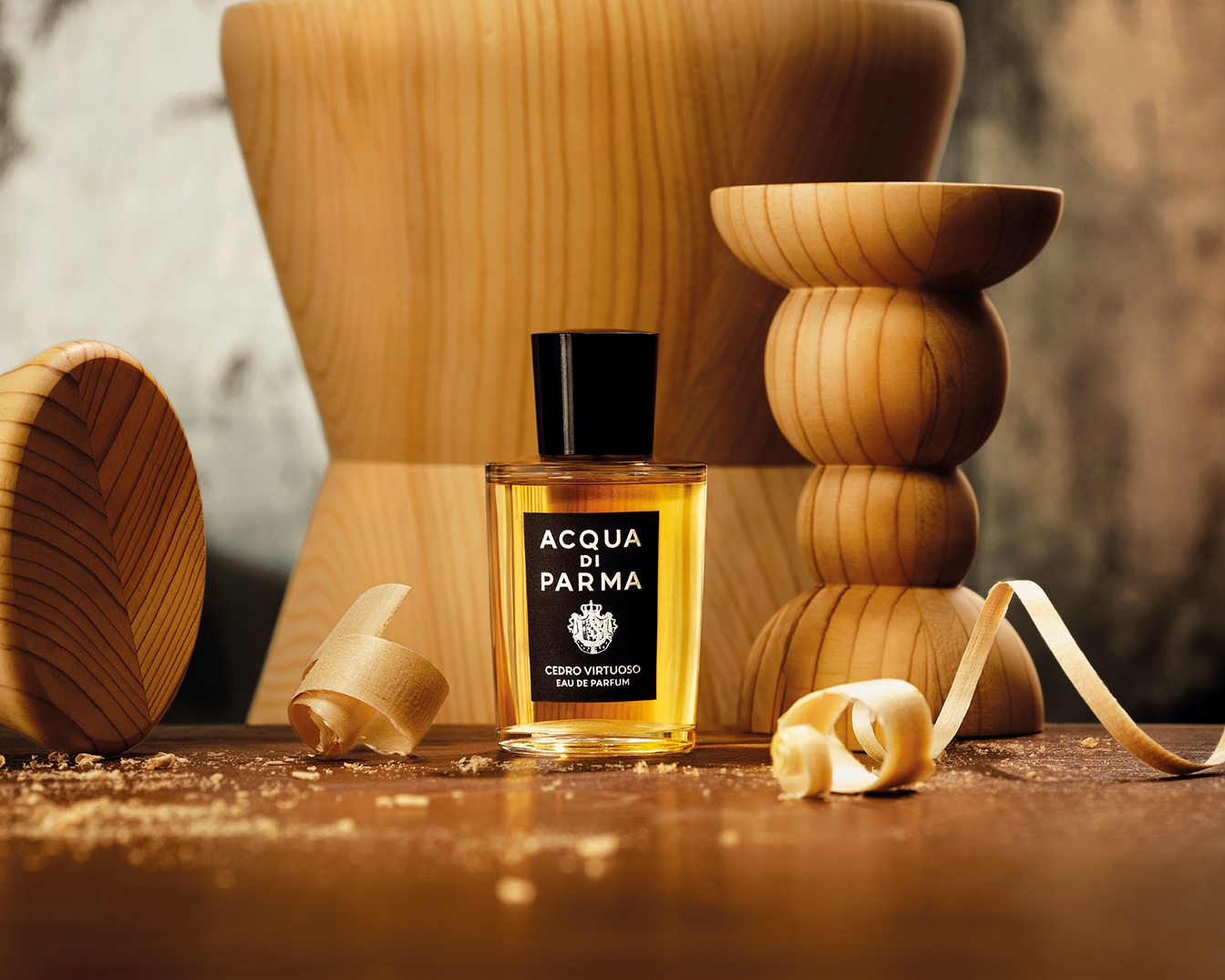 Perfumy Acqua di Parma Cedro Virtuoso Eau de Parfum w przezroczystej butelce z czarną nakrętką i etykietą, otoczone drewnianymi elementami i wiórkami, stoją na drewnianym blacie.
