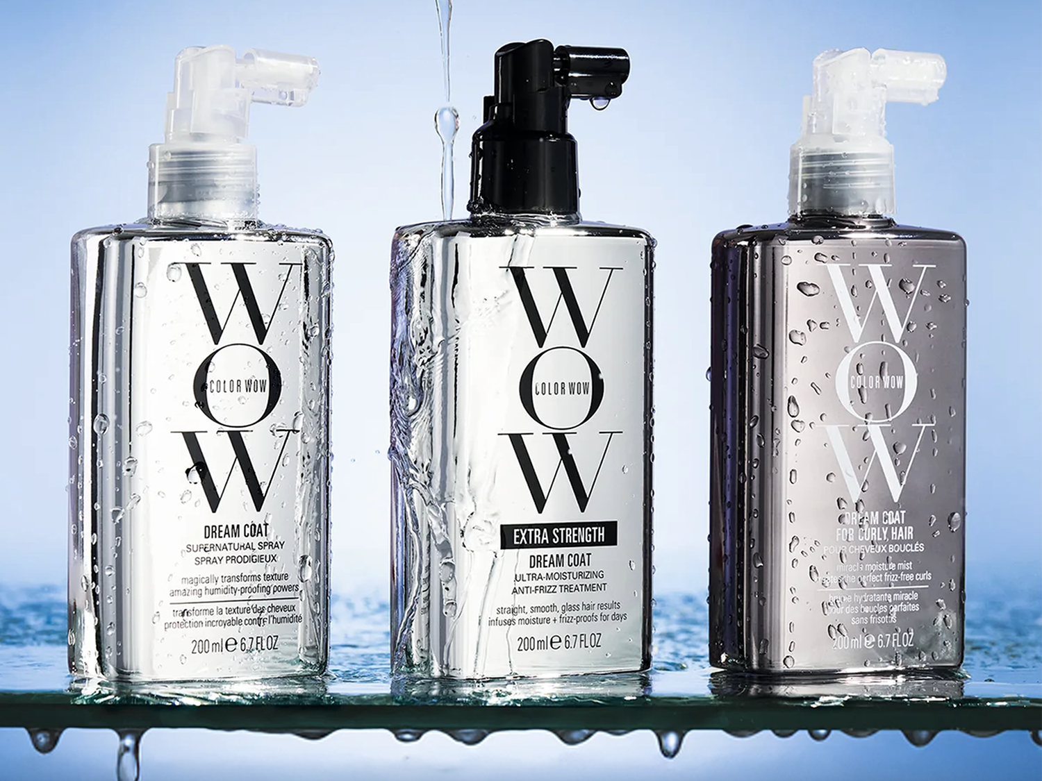 Drie flessen Color Wow Dream Coat haarproducten staan op een glazen plank, met waterdruppels die van bovenaf vallen en de flessen en het oppervlak bevochtigen.
