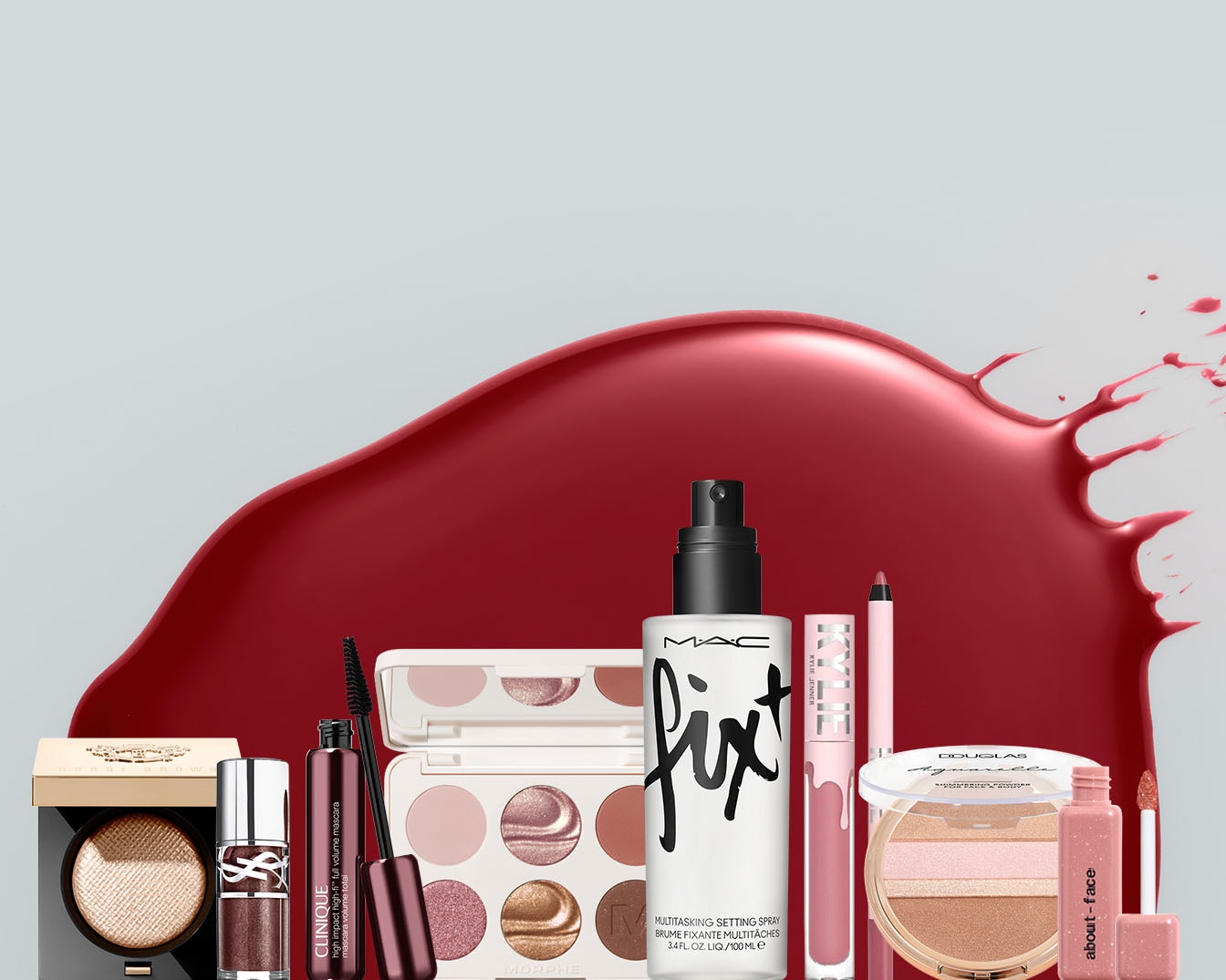 Różne produkty do makijażu, w tym tusz do rzęs Clinique High Impact High-Fi, spray utrwalający MAC Fix+, paleta cieni do powiek Morphe, błyszczyk Kylie Jenner, rozświetlacz Douglas i błyszczyk About-Face, są ułożone na tle czerwonej plamy, tworząc dynamiczną kompozycję.