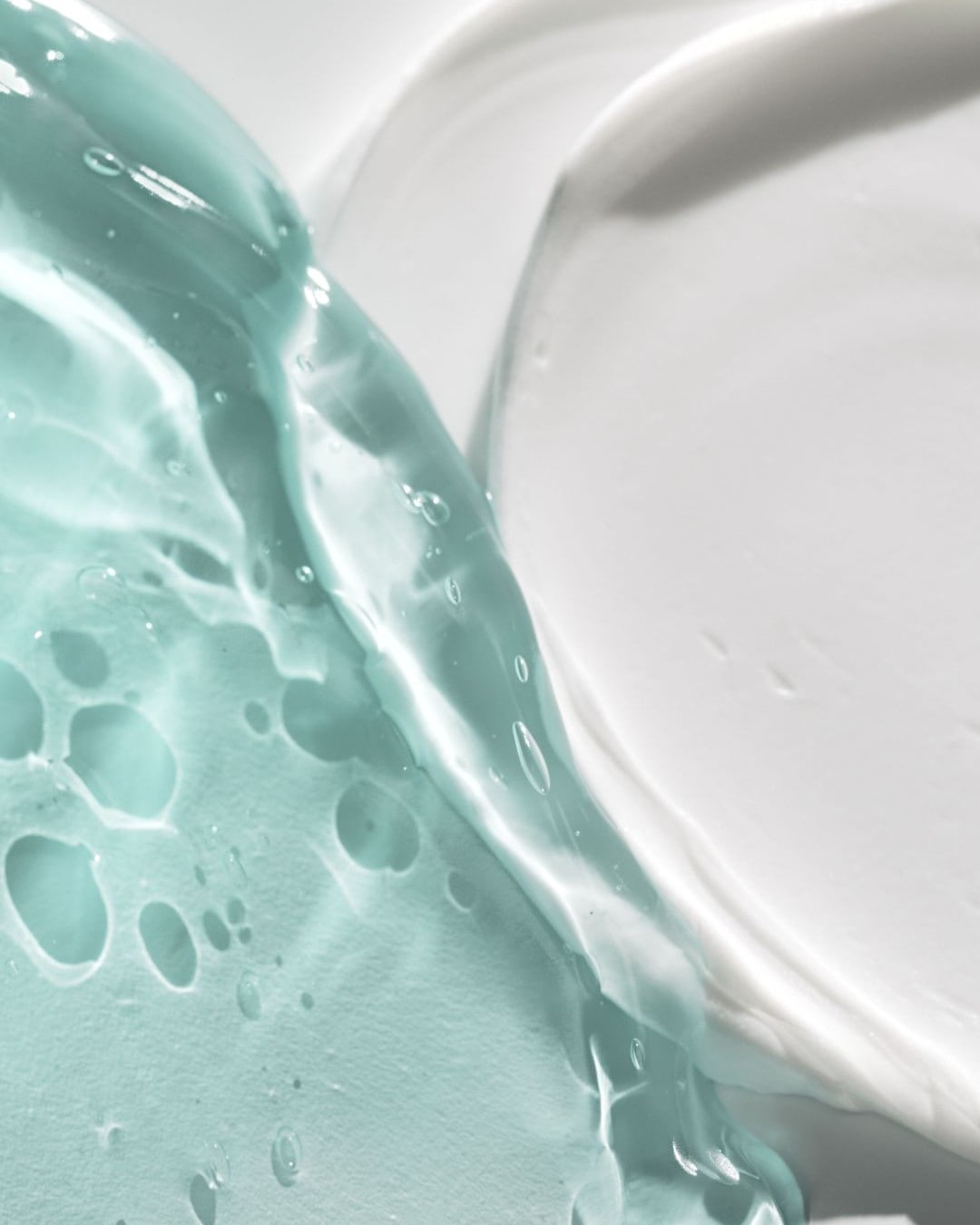Una texture di gel acquamarina e crema bianca si fondono, mostrando la consistenza liscia e idratante dei prodotti per la cura della pelle.