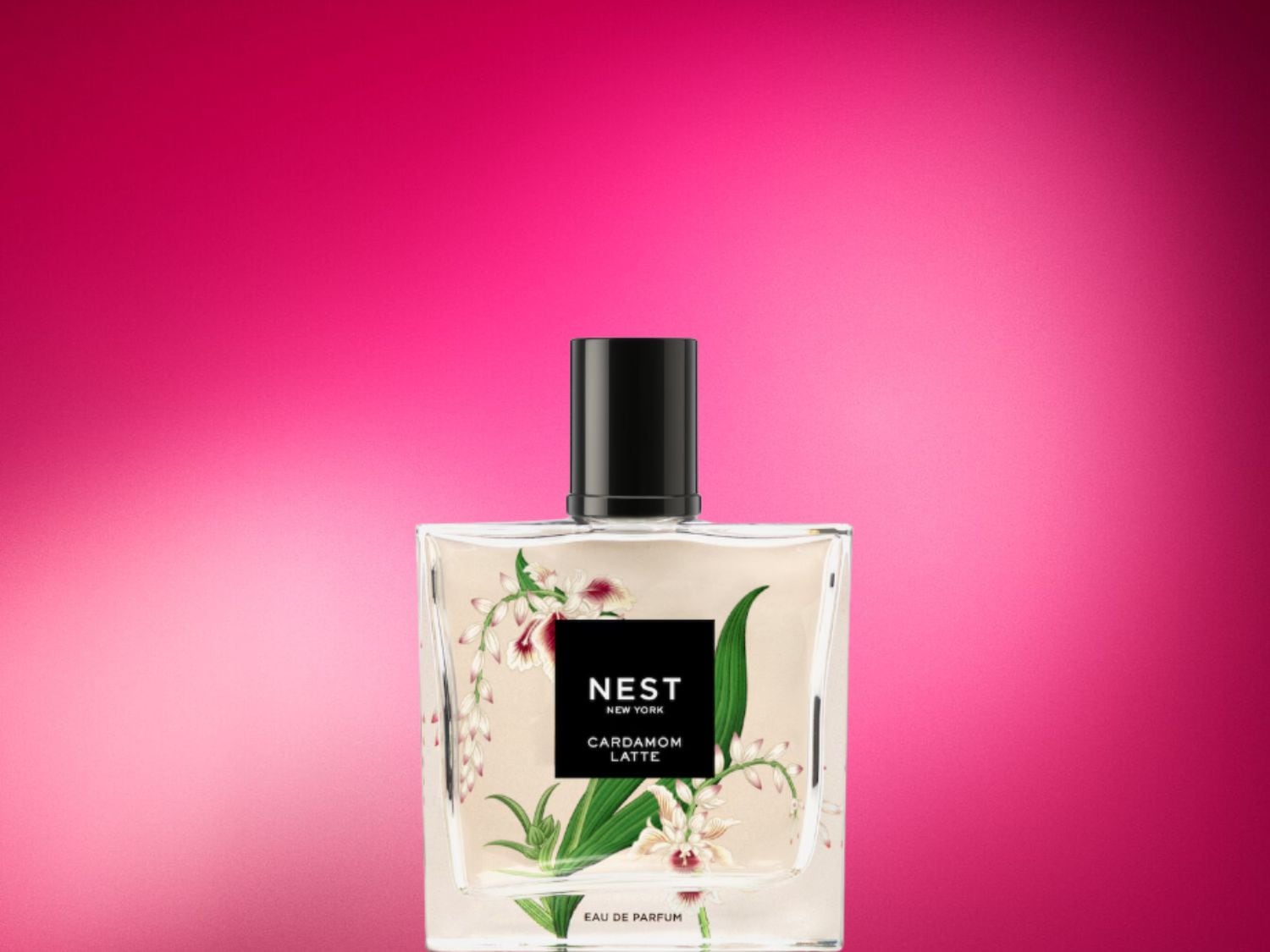Parfém Nest New York Cardamom Latte v hranaté skleněné lahvičce s černým uzávěrem, zdobený květinovým motivem, stojí na růžovém pozadí.