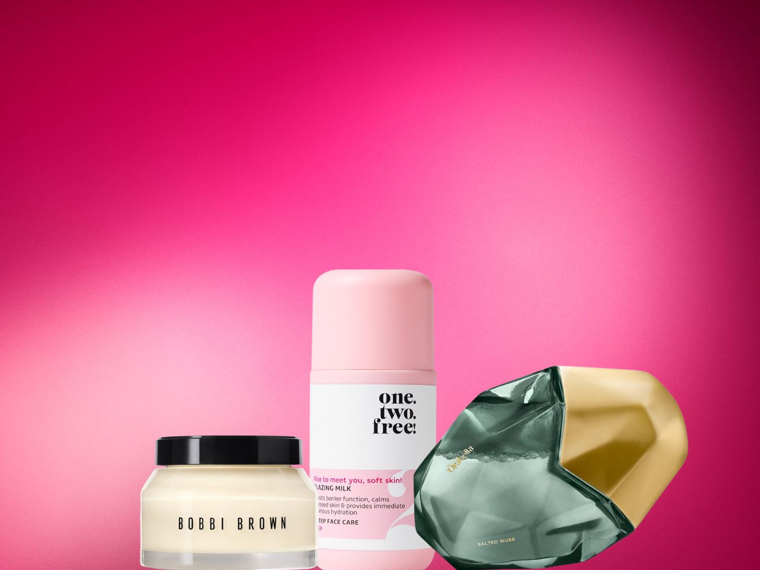 Tři kosmetické produkty jsou zobrazeny na zářivě růžovém pozadí: krém Bobbi Brown ve skleněné nádobce s černým víčkem, růžová lahvička One.Two.Free! Glazing Milk a parfém Orabella Salted Muse v zeleném a zlatém flakonu.