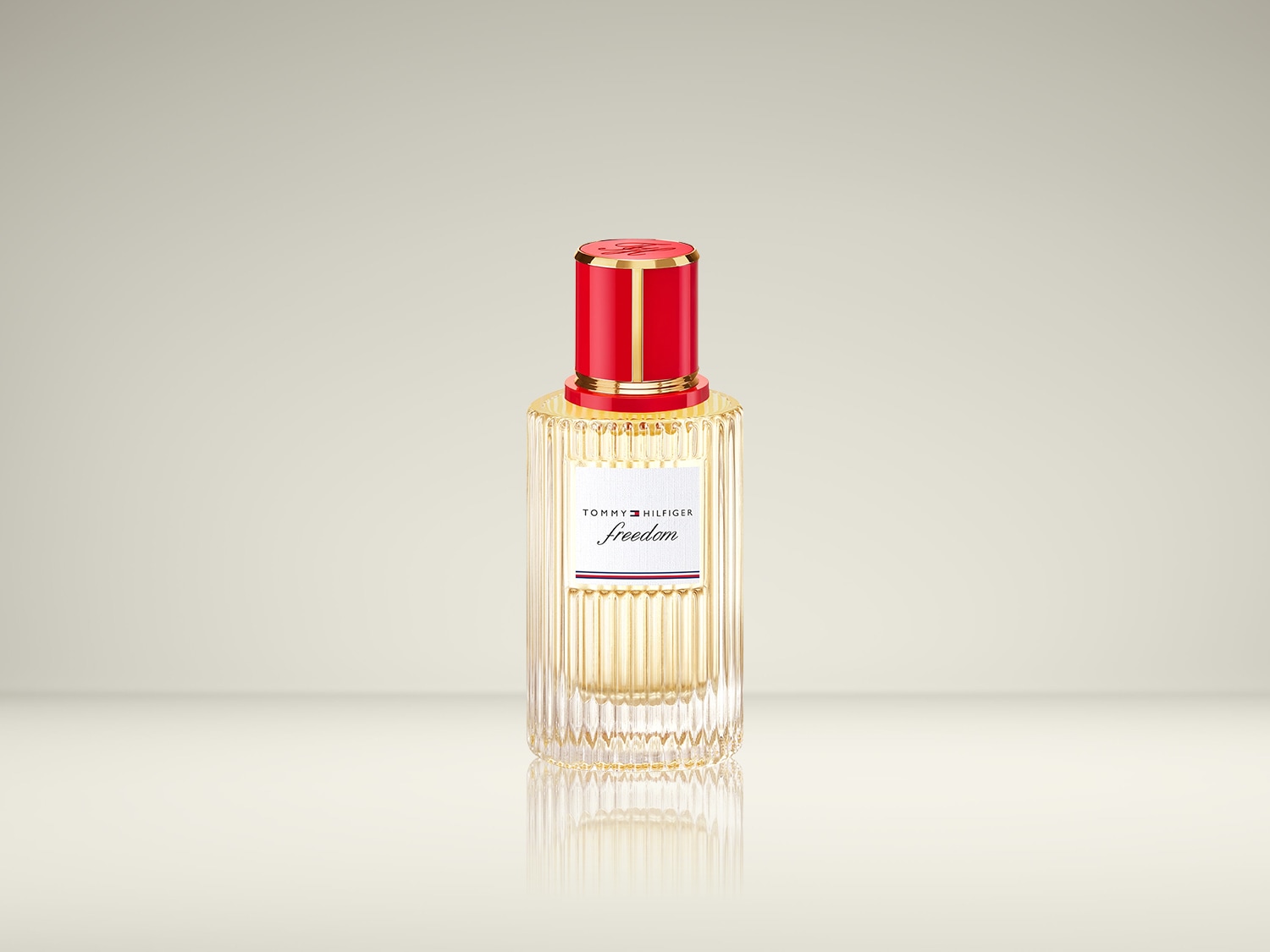 De Tommy Hilfiger Freedom parfumfles heeft een geribbelde glazen behuizing met een heldergele vloeistof en een opvallende rode dop met gouden accenten.