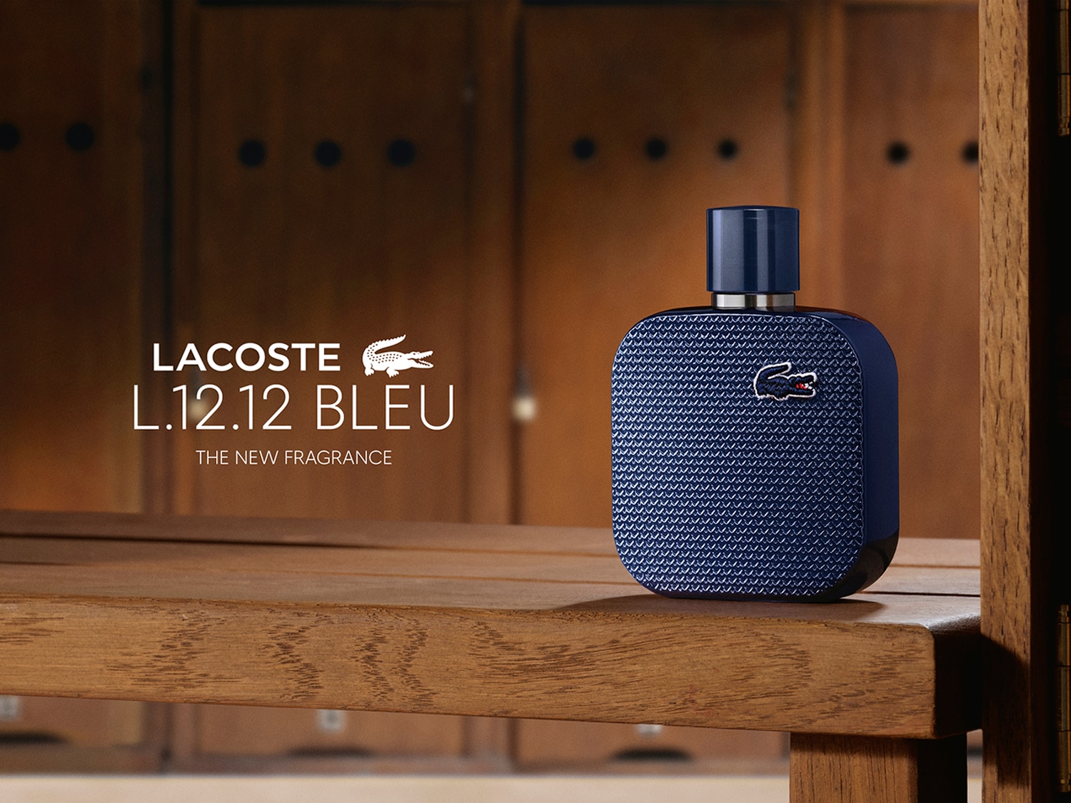 Flakon wody toaletowej Lacoste L.12.12 Bleu o głębokim, niebieskim kolorze i charakterystycznej strukturze pikowanego materiału stoi na drewnianej ławce, prezentując nowy zapach.