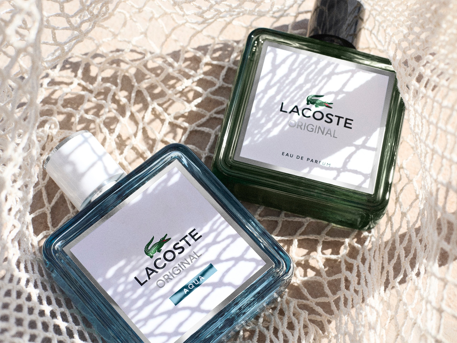 Dwa flakony perfum Lacoste Original w szklanych butelkach spoczywają na plecionej siatce, prezentując elegancki design i kultowe logo marki.