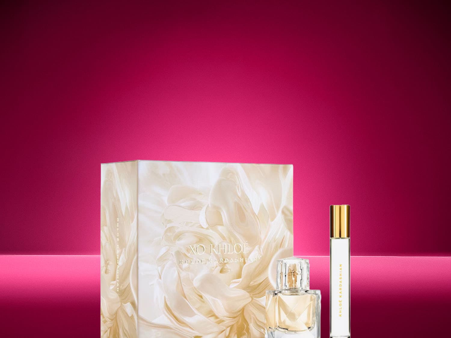 Ein edles XO Khloé Parfümset in einer marmorierten Geschenkbox, begleitet von einem klassischen Flakon und einem praktischen Taschenzerstäuber auf leuchtend pinkem Hintergrund.