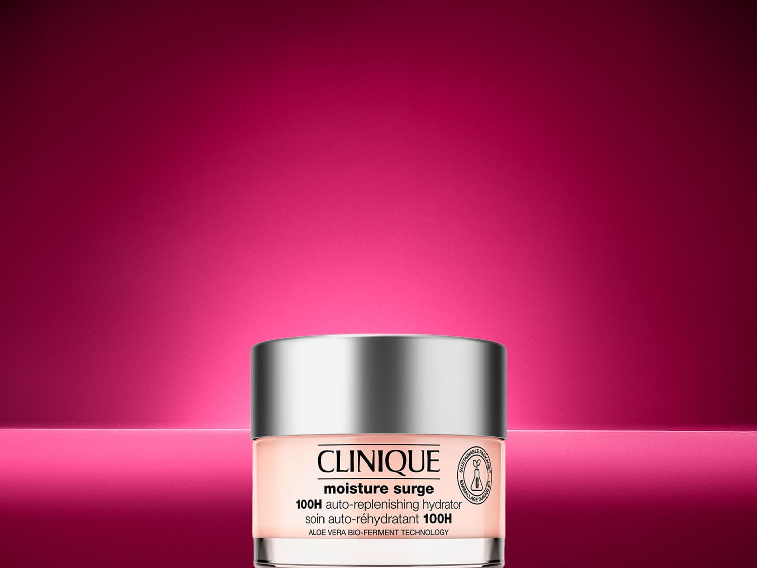 Der Clinique Moisture Surge 100H Auto-Replenishing Hydrator in einem runden Glasgefäss mit silbernem Deckel steht auf einer leuchtend pinken Oberfläche vor einem pinken Hintergrund. Jetzt entdecken!