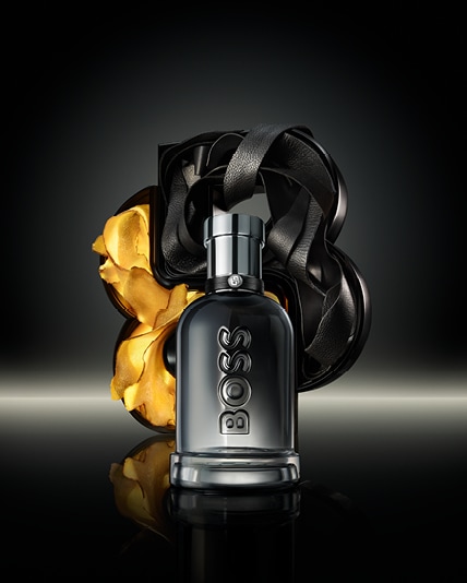 BOSS Bottled Beyond Flakon vor skulpturalem B-Logo aus schwarzem Lederband und Ingwer, stilvoll beleuchtet.