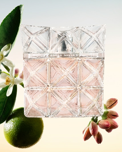 Facettenreich geschliffener, transparenter Parfümflakon Lumière d’Issey mit roséfarbener Flüssigkeit, umgeben von den Inhaltsstoffen des Duftes: grüner Mandarine, Moschus-Orangenblüte und Pistazienholz.