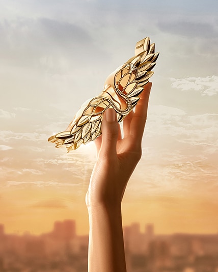 Eine Hand hält das Zadig L'intense in den Himmel mit Wolken und einer Stadt im Hintergrund.