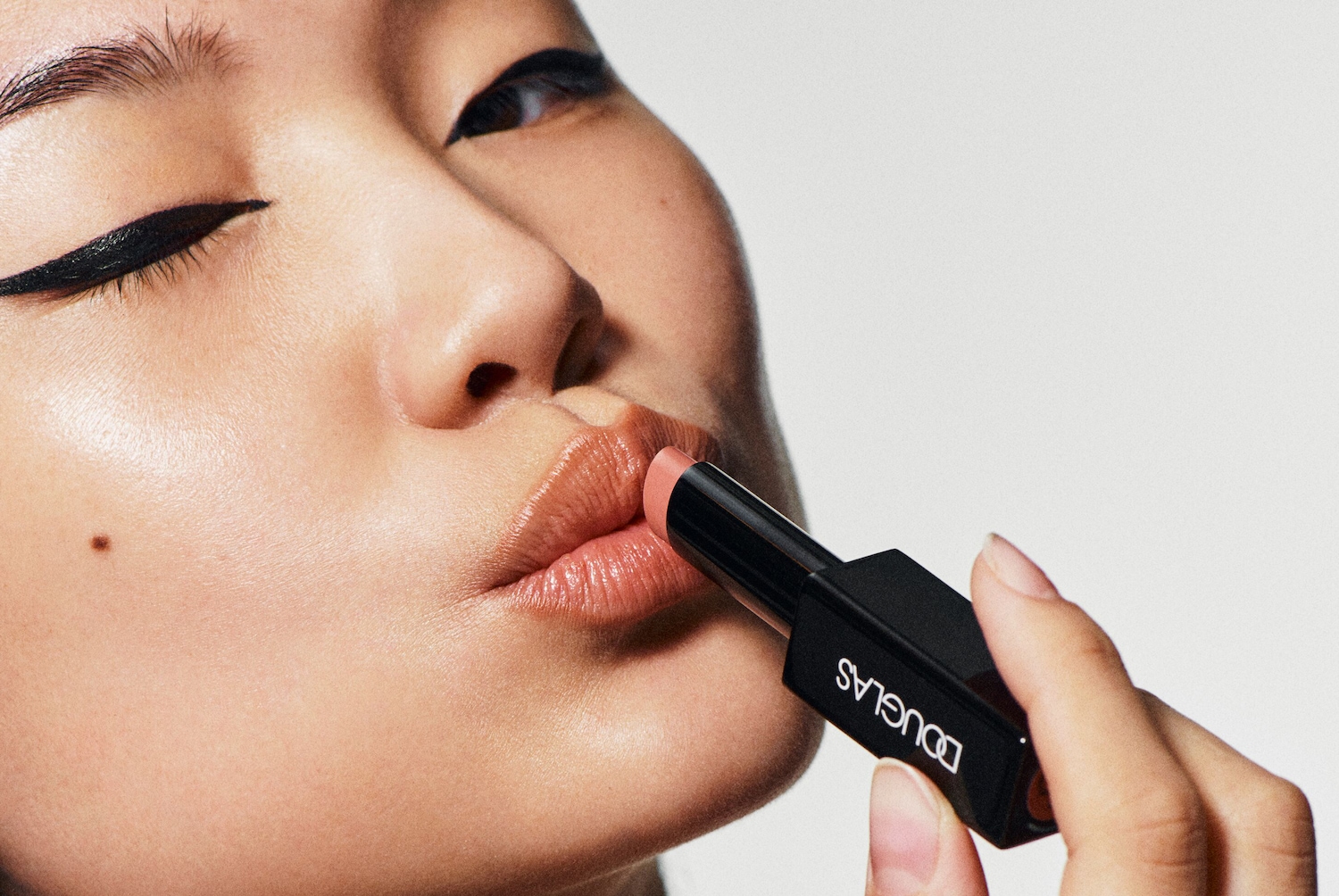 Een vrouw brengt een DOUGLAS-lippenstift aan terwijl ze met haar oog knipoogt.